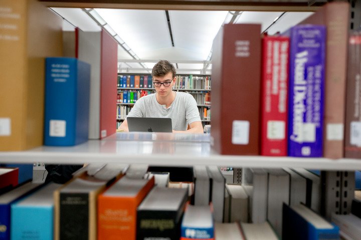 A male student works on his laptop in the library.